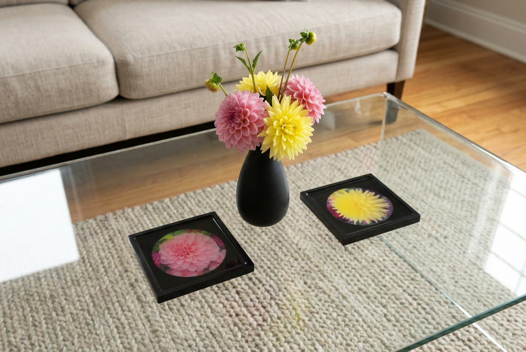 Two floral coasters on a glass coffee table with a black vase of fresh flowers between them